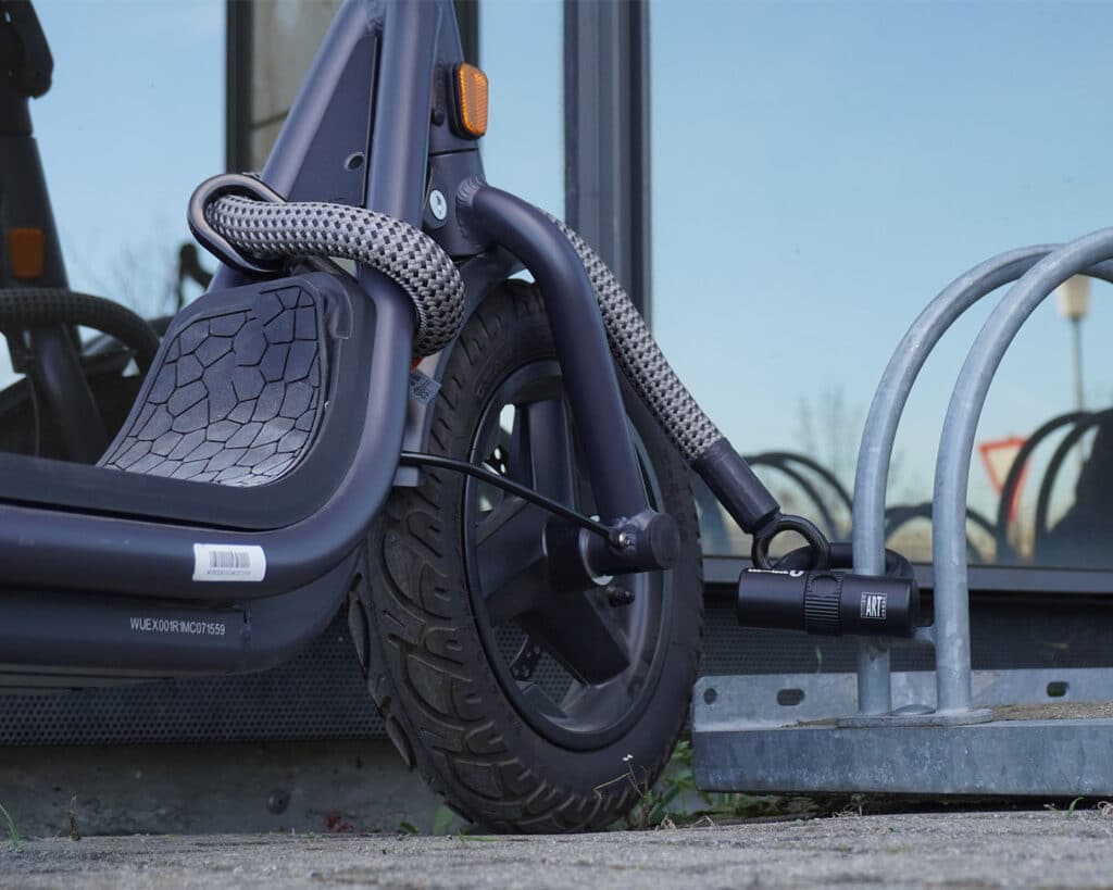 graue Bügelschloss-Verlängerung aus Textil sichert Roller mit Bügelschloss an Fahrradständer ab