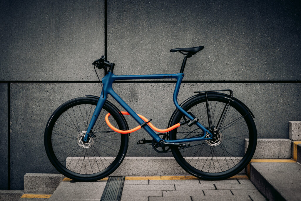 Blaues Fahrrad an grauer Mauer sicher abgeschlossen mit tex-lock eyelet orange