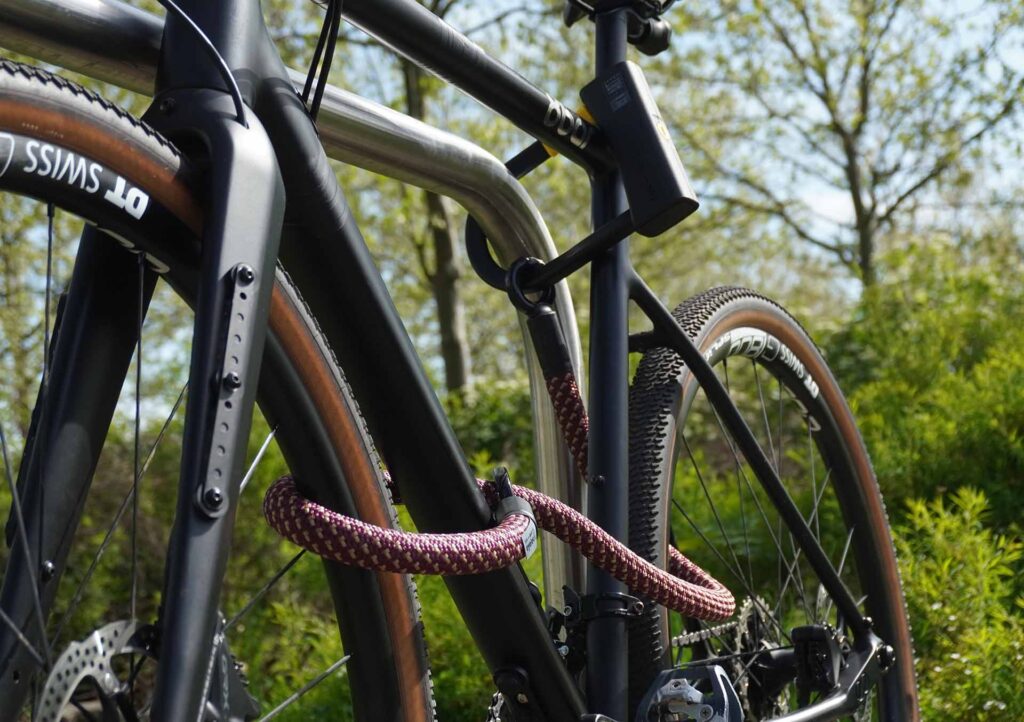 Fahrrad am Hinterrad, Vorderrad und Fahrradrahmen mit D-lock Bügelschloss und eyelet-Textilseil in chateau red am Fahrradständer angeschlossen
