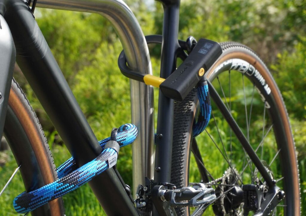 Fahrrad am Hinterrad, Vorderrad und Fahrradrahmen mit D-lock Bügelschloss und eyelet-Textilseil in morpho blue am Fahrradständer angeschlossen