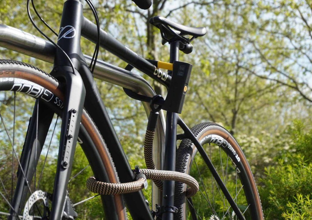 Fahrrad am Hinterrad, Vorderrad und Fahrradrahmen mit D-lock Bügelschloss und eyelet-Textilseil in wild hemp am Fahrradständer angeschlossen