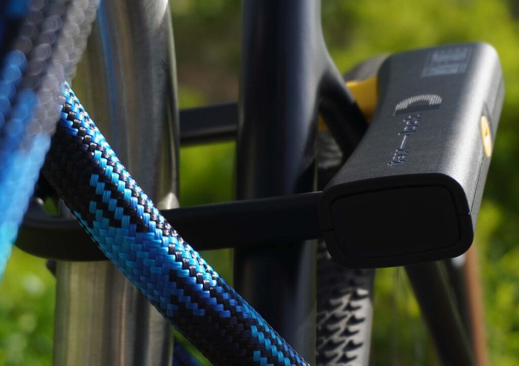 D-lock Bügelschloss sichert Sattelstange und Sattelstrebe mit Textilseil in Farbe morpho blue am Fahrradständer