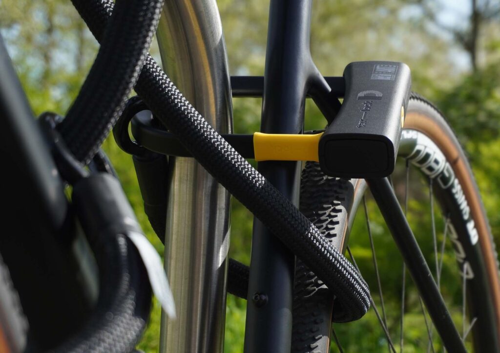 D-lock Bügelschloss sichert Sattelstange und Sattelstrebe mit Textilseil in Farbe onyx black am Fahrradständer