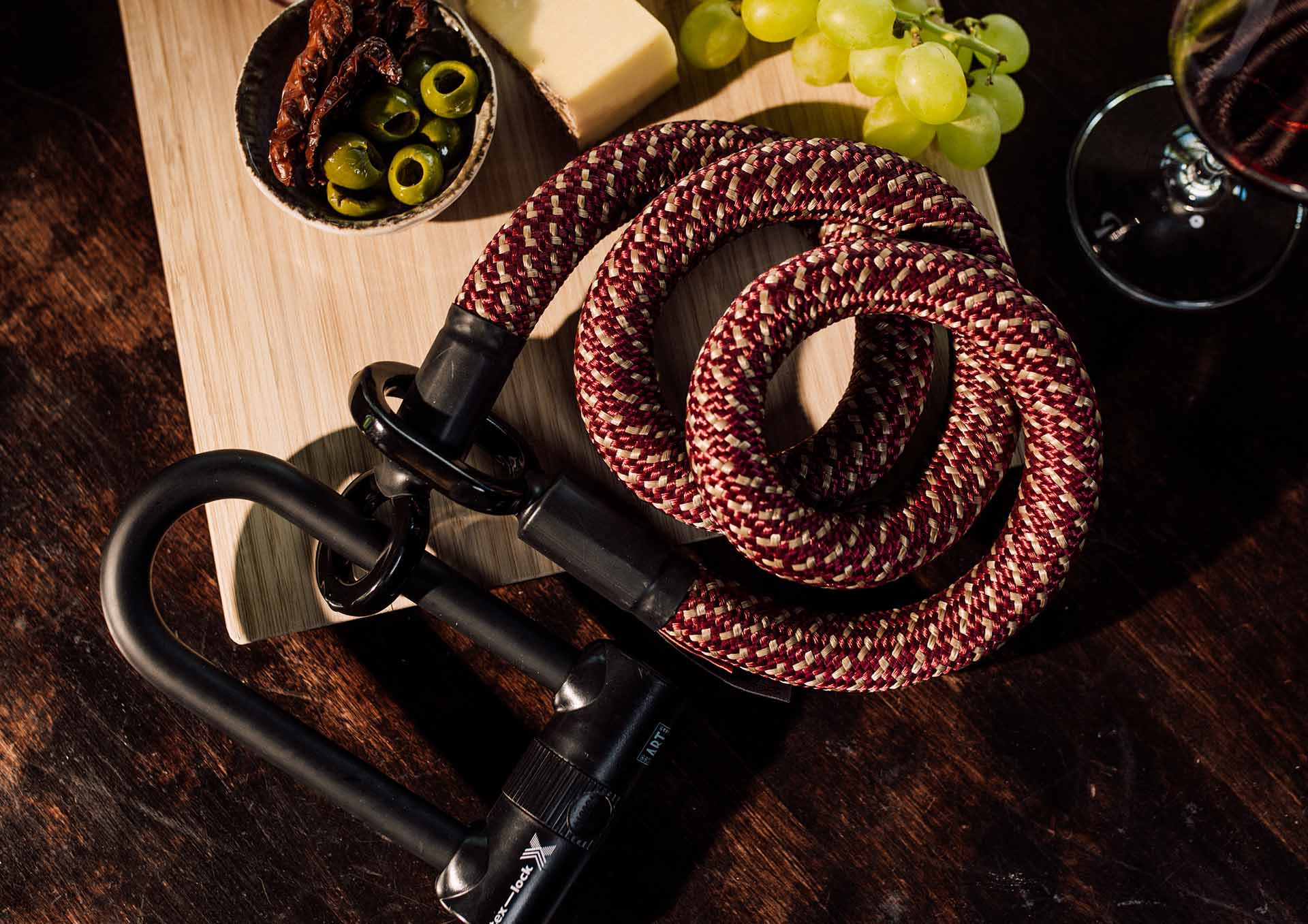tex–lock eyelet in chateau red mit X-lock liegt zusammengewickelt auf einem Holzbrett mit Antipasti und Rotwein