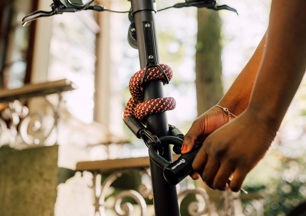 Frau öffnet tex–lock eyelet in chateau red mit U-lock das flexibel um die Lenkstange vom E-Scooter gewickelt ist