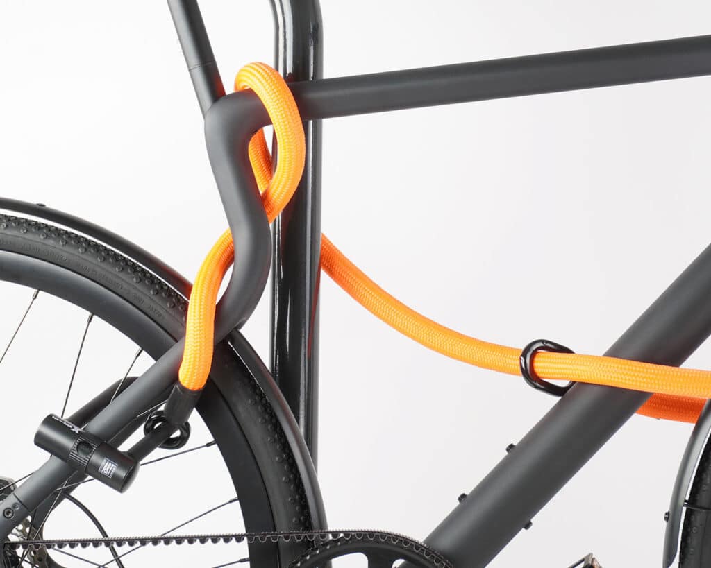 Bügelschloss mit Verlängerung aus Textil in orange sichert Vorder-, Hinterrad und Rahmen gleichzeitig am Fahrradständer ab