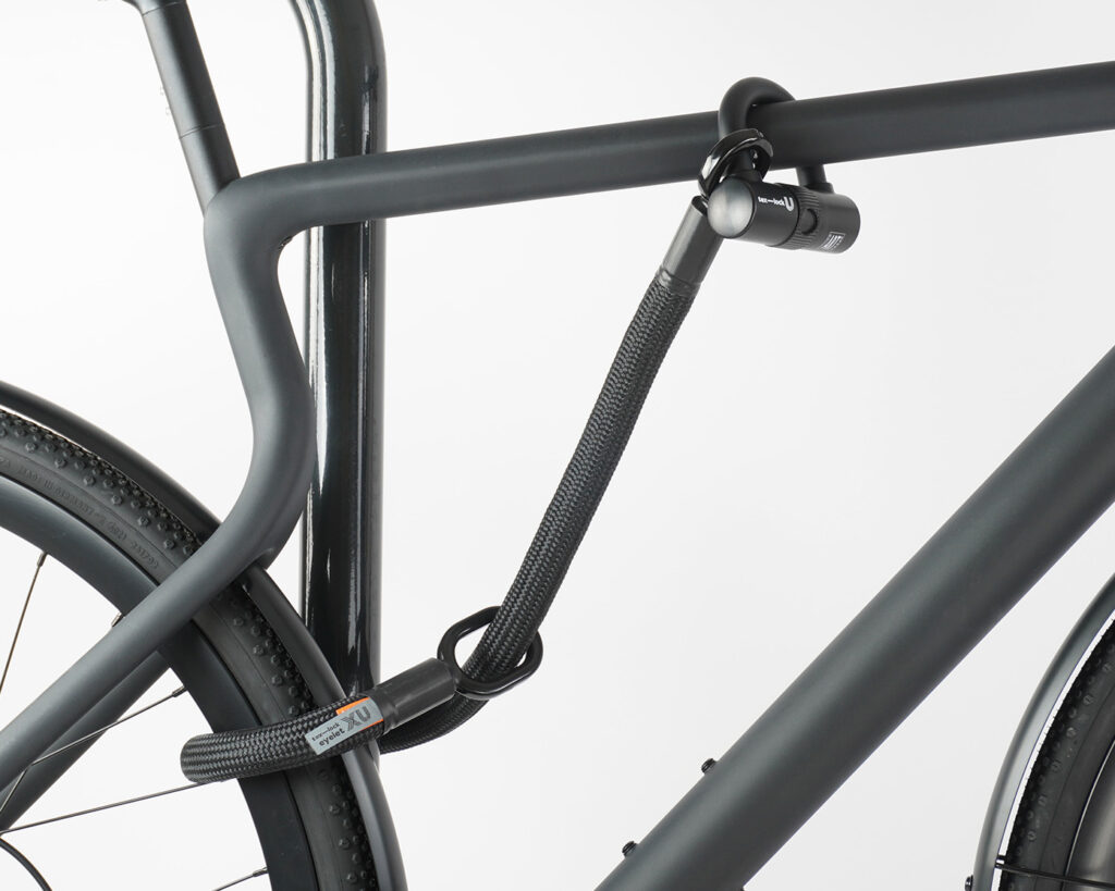 Hinterrad und Oberrohr vom Fahrrad mit Bügelschloss und Verlängerung aus Textil in schwarz am Fahrradständer angeschlossen