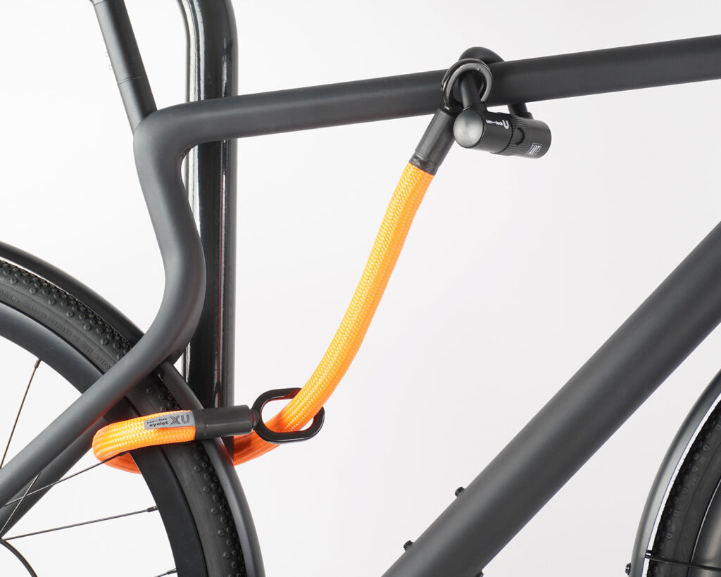 Hinterrad und Oberrohr vom Fahrrad mit Bügelschloss und Verlängerung aus Textil in orange am Fahrradständer angeschlossen