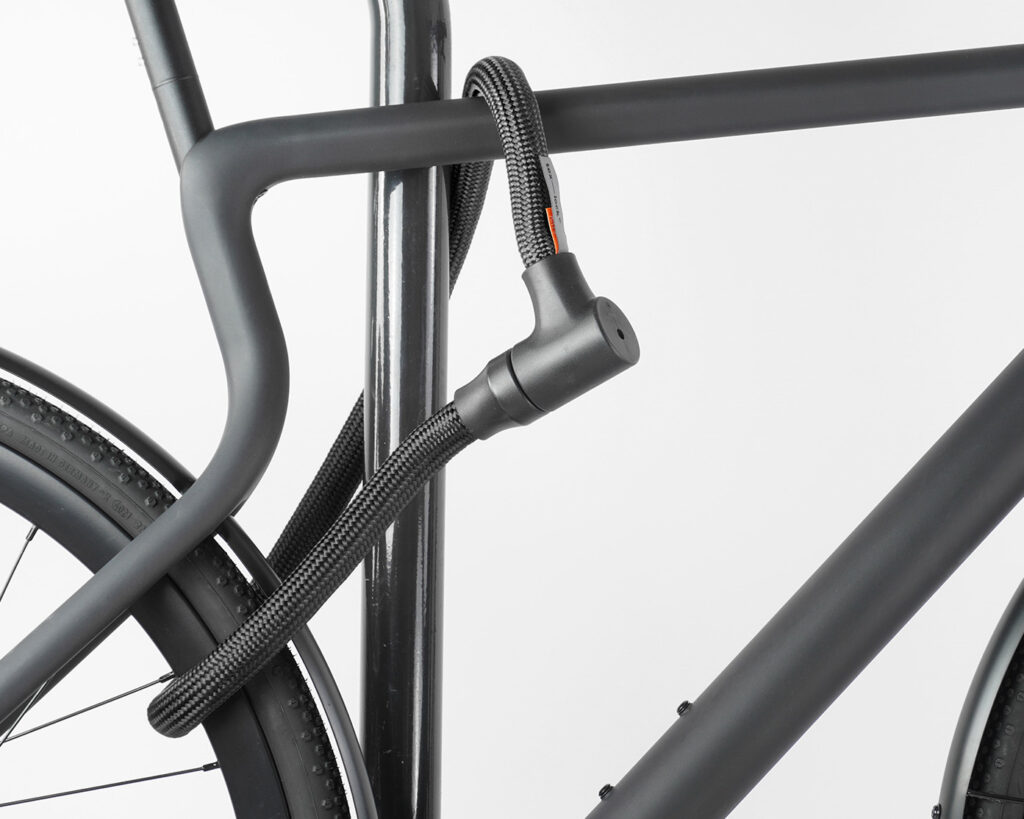 Hinterrad und Oberrohr vom Fahrrad mit schwarzem Seilschloss aus Textil an Fahrradständer angeschlossen