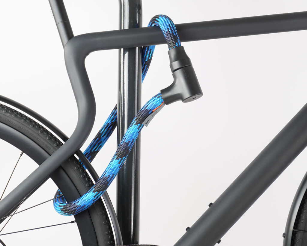 Hinterrad und Oberrohr vom Fahrrad mit blau-schwarzem Seilschloss aus Textil an Fahrradständer angeschlossen