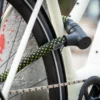 Schwarzes Fahrradschloss mit Neonmuster um das Hinterrad und das Unterrohr eines weißen Fahrrads gewickelt