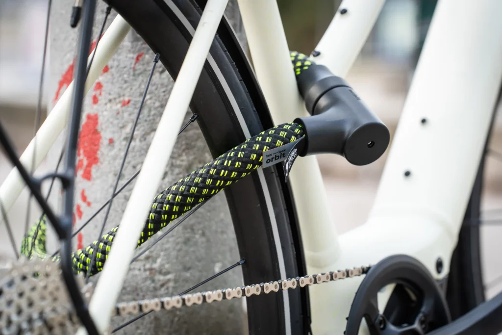 Schwarzes Fahrradschloss mit Neonmuster um das Hinterrad und das Unterrohr eines weißen Fahrrads gewickelt