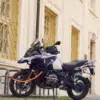 tex–lock eyelet in acid orange sichert Motorrad mit U-lock an Fahrradständer vor gelbem Haus