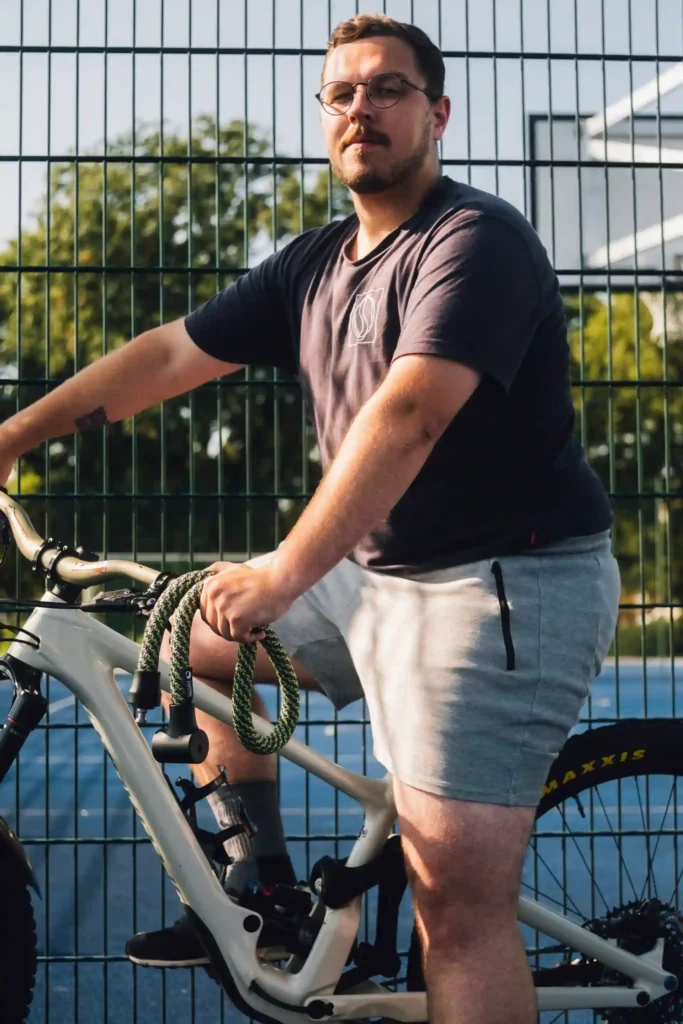 Mann in T-Shirt und kurzer Hose auf Fahrrad mit tex–lock orbit one spirit in der Hand